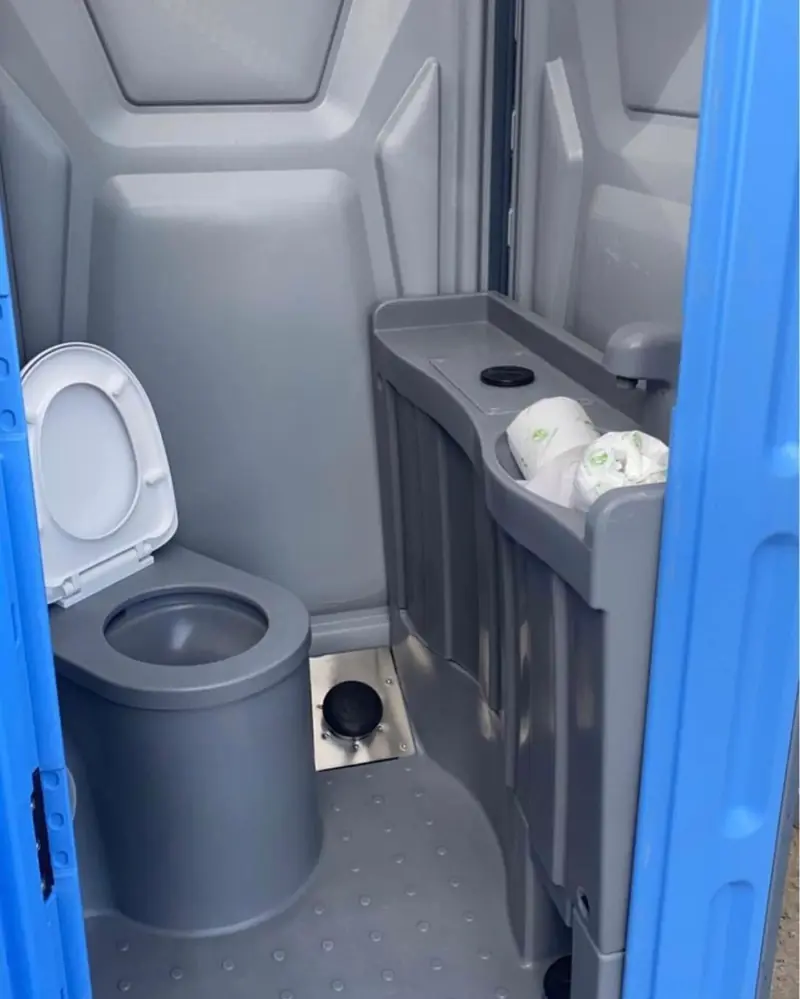 Deluxe flushable portable toilet interior with a lidded toilet seat, flush pedal and stocked paper shelf