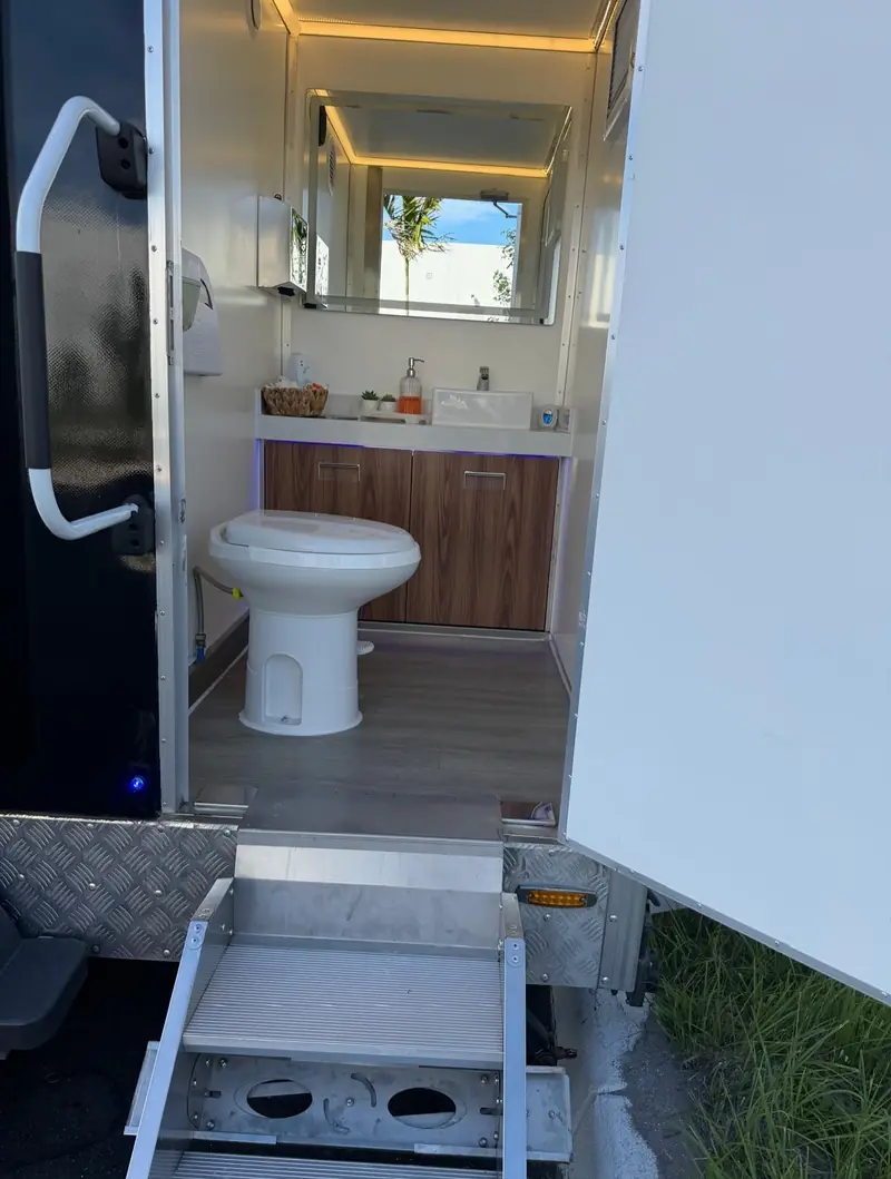 Luxury restroom trailer stall with porcelain-style toilet, wood vanity and LED mirror